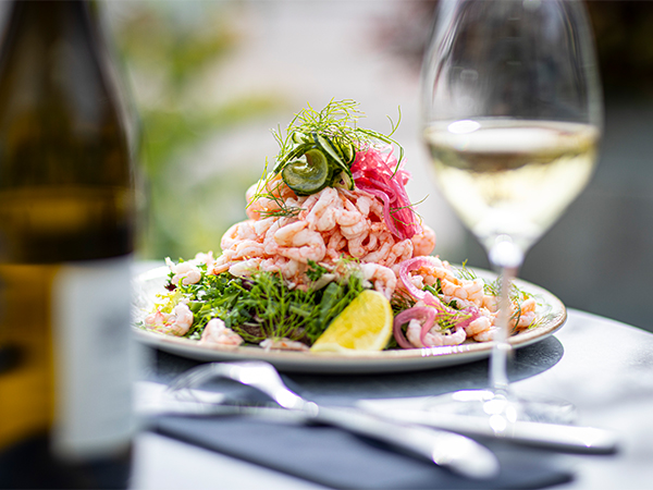 Tallrik med räkmacka, citron och dill, serverad med ett glas vitt vin.